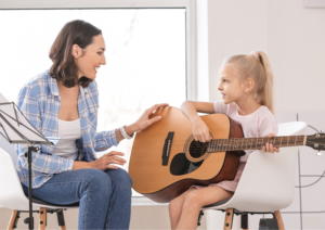 female guitar teacher is teaching guitar to a happy girl enjoying her lessons