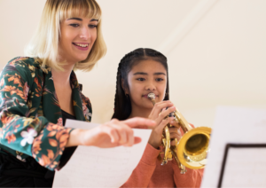 happy music teacher teaching trumpet to a girl