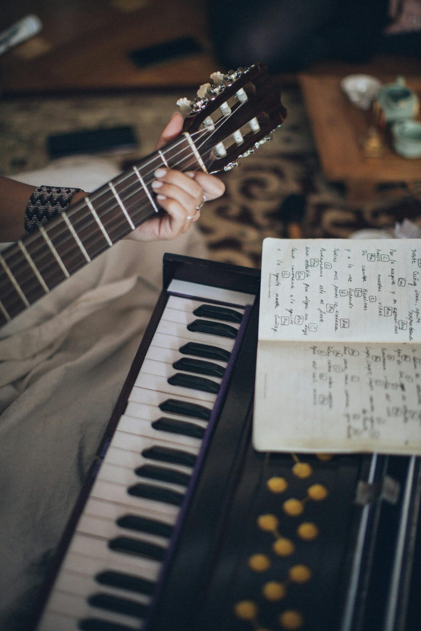 Close-up view of a guitar and keyboard with sheet music, capturing a cozy indoor music session.